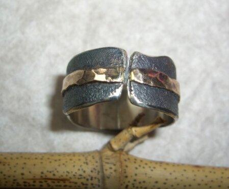 Silberring mit breiter Goldwelle Ring, dessen Front offen gehalten ist. Geschmort und mit umlaufender, breiter Goldwelle. Breite 10 mm.<br />Ringgroesse nach Wunsch.