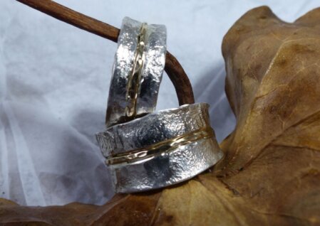 Trauringe mit 333er Goldeinsatz Trauringe mit ¾ umlaufendem 333 Goldeinsatz. Geschmorte Oberflaeche. Breite optional waehlbar. Abgebildet: 10 mm und 7 mm.